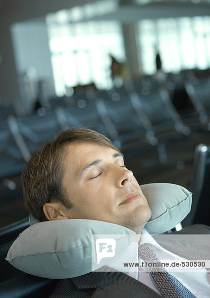 Mann ruht mit Nackenkissen in der Flughafenlounge