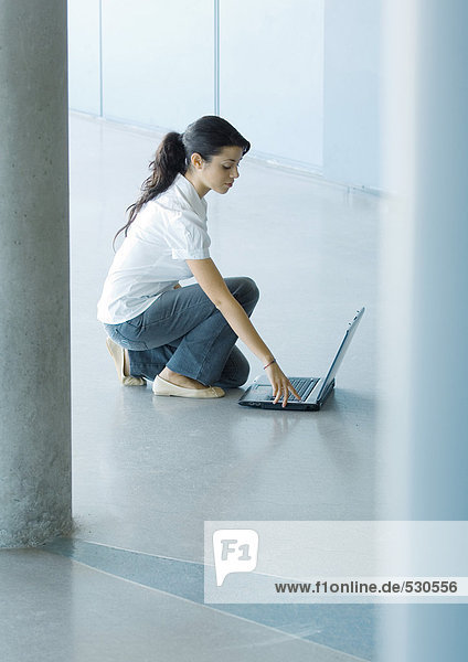 Junge Frau auf dem Boden hockend  mit Laptop