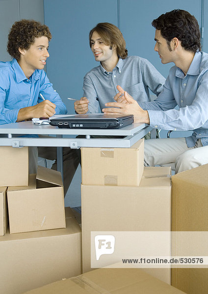 Businessmen talking  sitting at table top supported by cardboard boxes