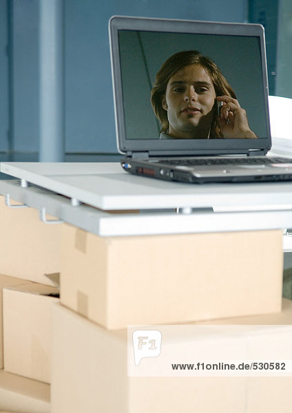 Bild des Mannes auf dem Laptop-Bildschirm  Laptop auf dem Tisch unterstützt von Pappkartons