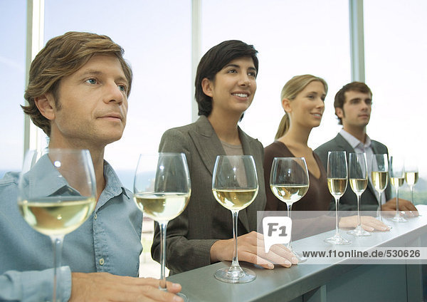 Vier Erwachsene stehen in Reihe mit Händen an der Bar  Gläser Wein vor ihnen.