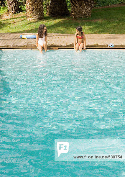 Two girls sitting on edge of swimming pool