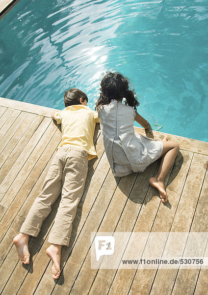 Boy and girl sitting at edge of swimming pool  high angle view
