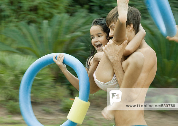 Adolescent boy carrying little sister  holding swimming ring