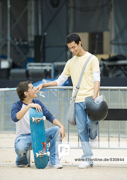 Teenager Rüden  einer mit Skateboard  der andere hält den Helm.