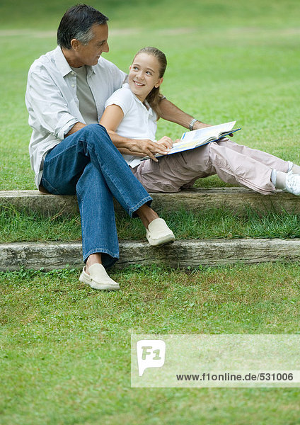 Mature man reading with granddaughter outdoors