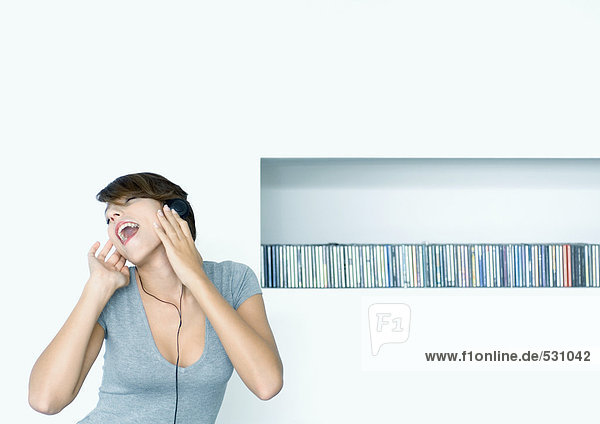 Frau hört Kopfhörer  CD-Regal im Hintergrund