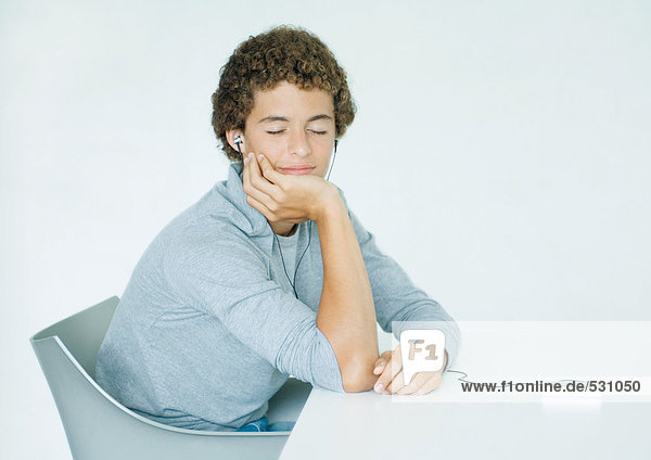 Junger Mann sitzt am Tisch und hört sich einen tragbaren MP3-Player an.