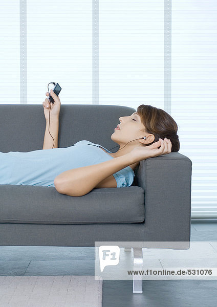 Junge Frau liegt auf dem Sofa und hört den tragbaren MP3-Player.