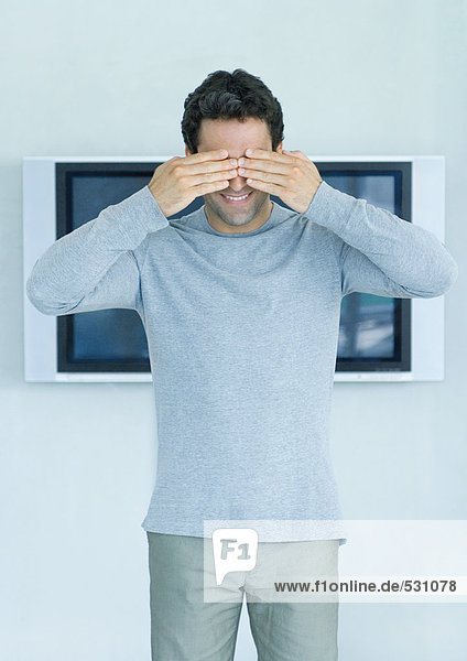 Mann steht vor Widescreen-TV an der Wand  Hände bedecken Augen