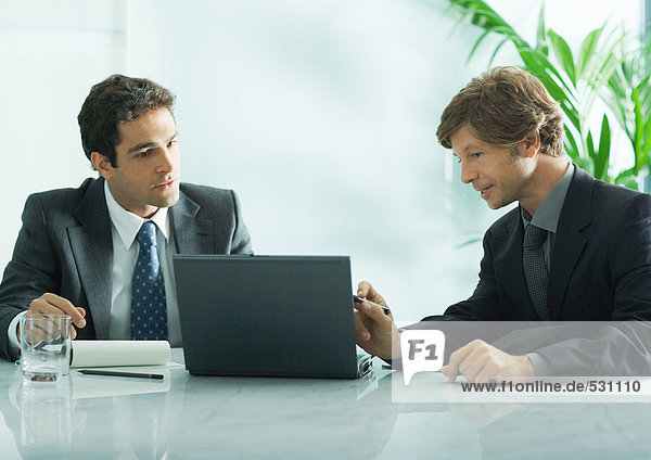 Two businesmen sitting at table  looking at laptop
