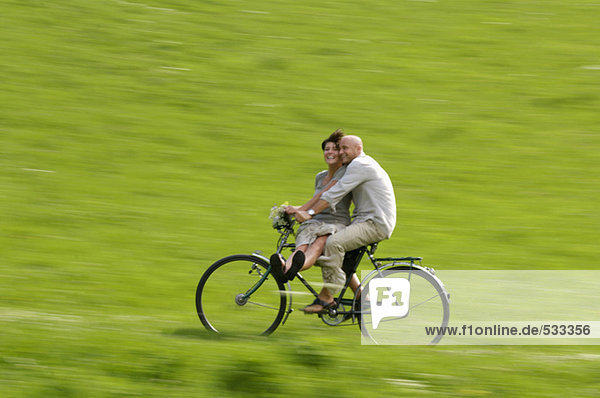 Couple riding bicycle in meadow