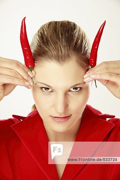 Junge Frau hält Chili auf dem Kopf  simuliert Hörner  Portrait