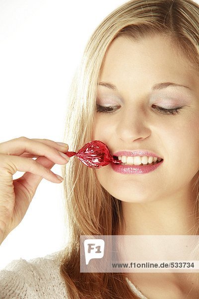 Junge Frau hält eingewickelte Süßigkeiten zwischen den Zähnen  Nahaufnahme