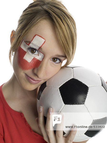 Junge Frau mit Schweizer Fahne auf Gesicht gemalt und Fußball haltend  Porträt