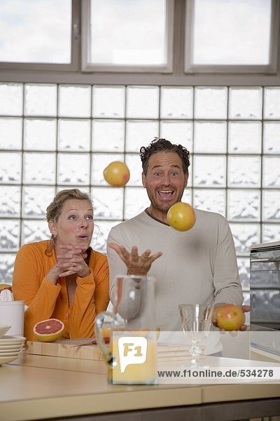 Mature couple in kitchen  Man juggling with grapefruits