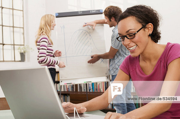 Young man explaining woman chart in background  focus on woman using laptop  smiling