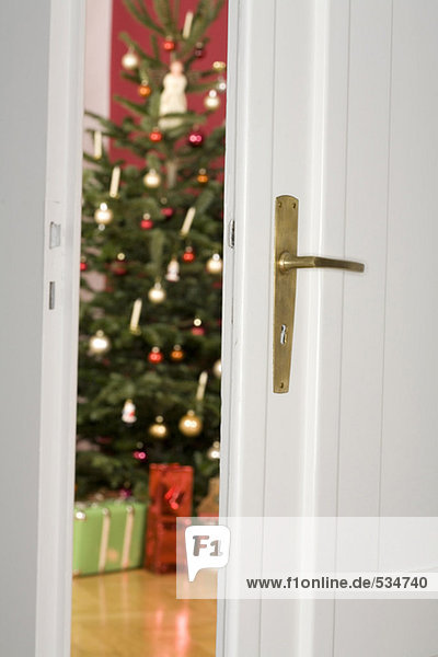 Blick durch die offene Tür zum Weihnachtsbaum und Geschenke