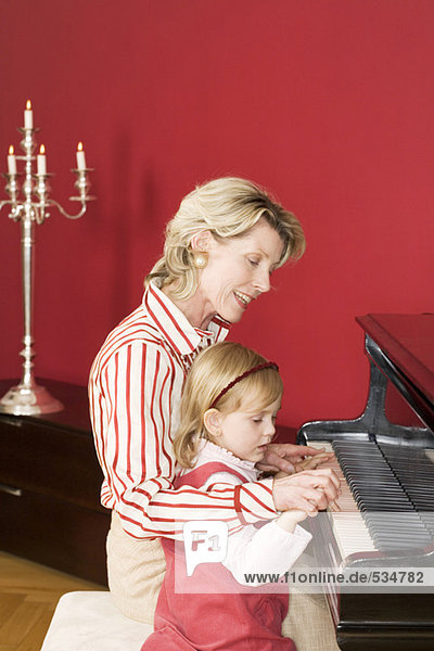 Großmutter und Enkelin (3-5) am Klavier sitzend  Seitenansicht