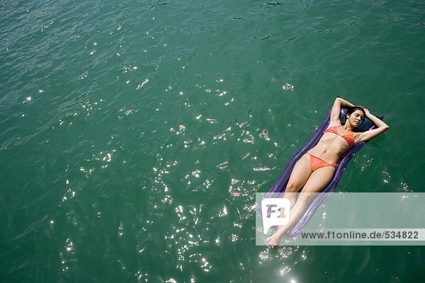 Junge Frau entspannt auf Luftmatratze  im Wasser schwimmend