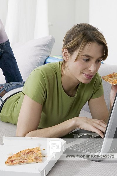 Junge Frau isst Pizza bei der Arbeit am Computer
