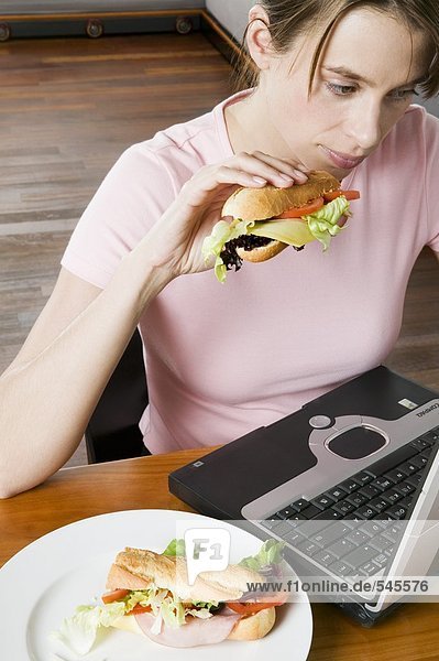 Junge Frau isst Sandwich bei der Arbeit am Computer