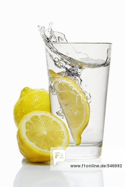 Eine Zitronenspalte fällt in ein Glas Wasser