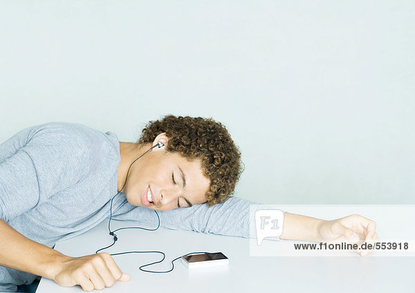 Teenager-Junge hört MP3-Player  Kopf liegt auf Arm und Augen geschlossen