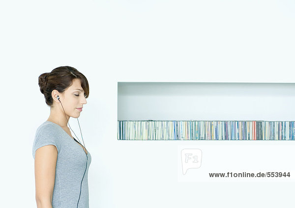 Junge Frau stehend  Kopfhörer hörend  neben CD-Reihe  Augen geschlossen