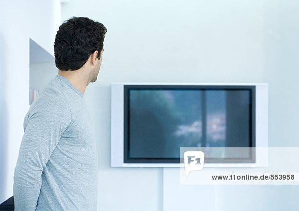 Mann blickt auf Flachbildfernseher an der Wand