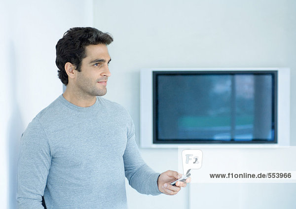 Mann hält Handy aus  schaut weg  Breitbild-TV im Hintergrund
