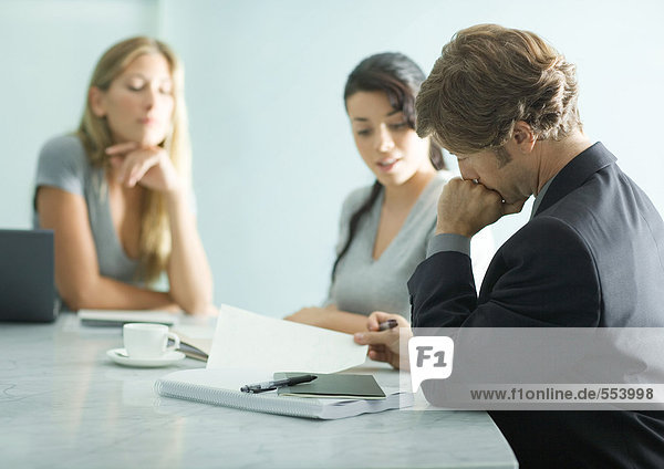 Mature man sitting at table with teenage girl and young female professional  reading document