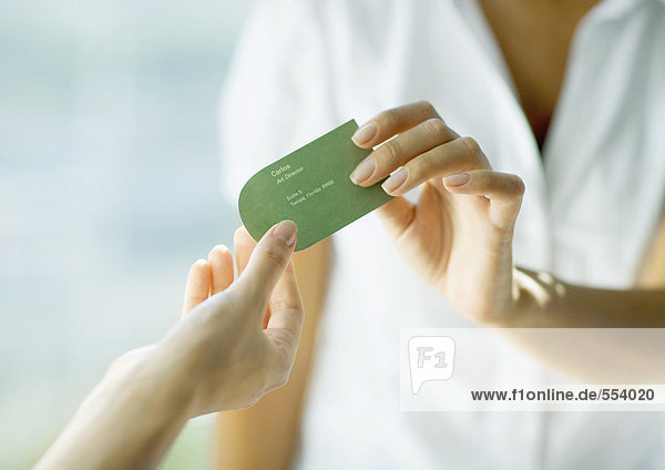 Woman handing second woman business card  close-up of hands
