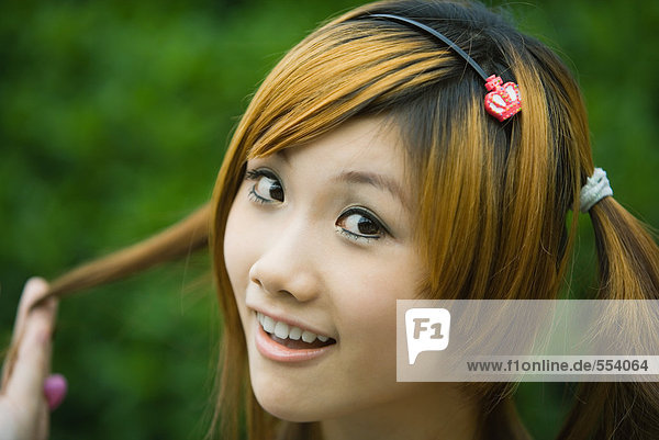 Young woman holding pigtail and smiling at camera  close-up  portrait