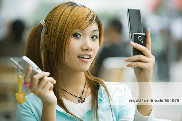 Young woman holding two cell phones  looking at camera