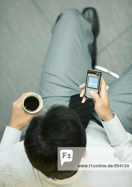 Geschäftsmann mit Smartphone  der eine Tasse Kaffee hält.