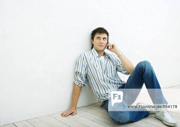 Junger Mann  der auf dem Boden sitzt und ein Handy benutzt.
