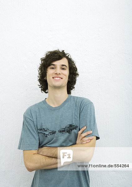 Junger Mann mit verschränkten Armen  lächelnd vor der Kamera  Portrait  weißer Hintergrund