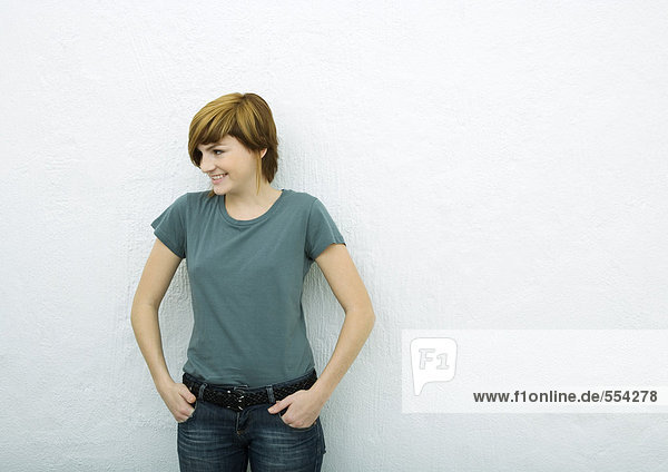Young woman standing with hands in pockets  looking away  white background