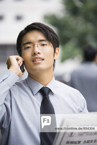 Businessman with newspaper using cell phone  looking at camera