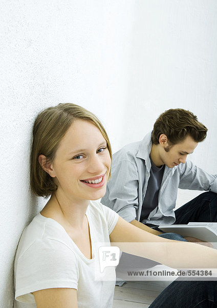 Teenage girl and young man sitting on floor  girl smiling at camera