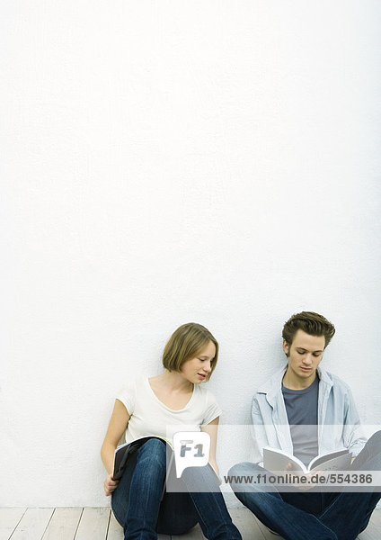 Teenage girl and young man sitting on floor with books  girl looking over at man's book