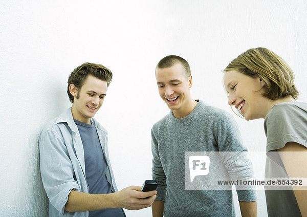 Drei junge Freunde  die das Handy anschauen  lächelnd