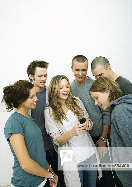 Group of young adult and teenage friends looking at cell phone  white background