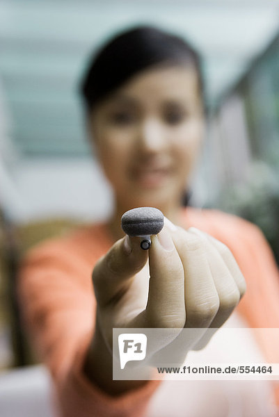 Young woman holding up earphone  focus on hand in foreground