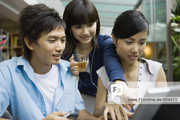 Drei junge Erwachsene mit dem Laptop  einer zeigt auf den Bildschirm.