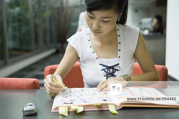Young woman marking book with adhesive notes