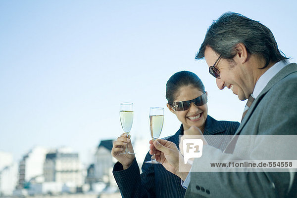 Business partners holding up glasses of champagne  skyline in background