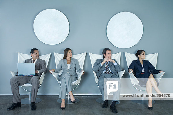 Business executives sitting in row of chairs  looking out of frame
