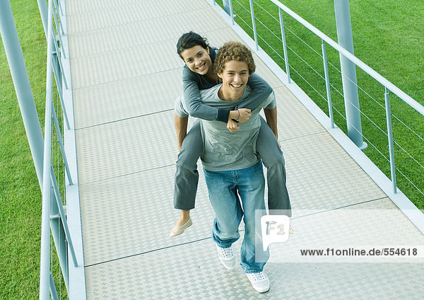 Teenage couple  boy carrying girl piggyback on walkway  smiling at camera